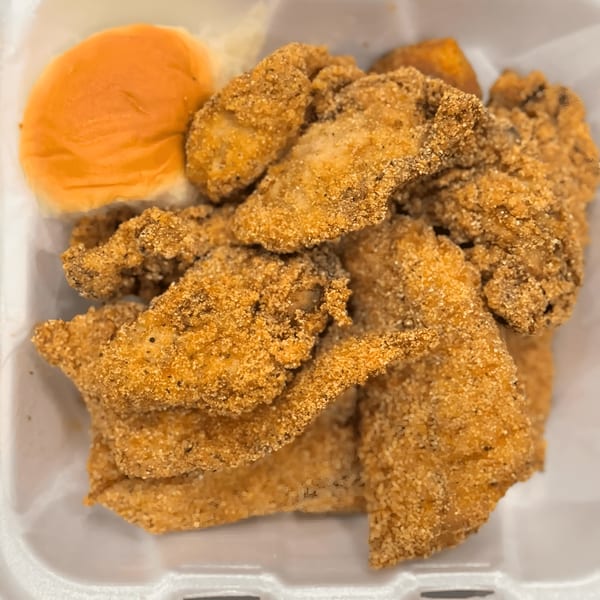 Golden-fried fish fillets and a soft dinner roll in a white takeout container from Fishbone Seafood.