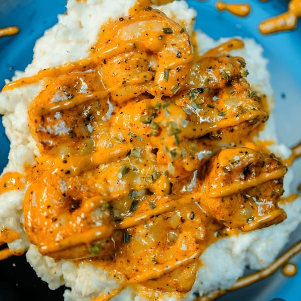 Shrimp and grits from Fishbone Seafood, with orange sauce and green herbs on a blue plate.